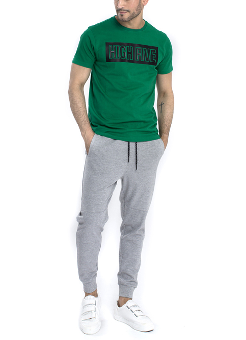 Model wearing green design shirt with grey jogger pants.